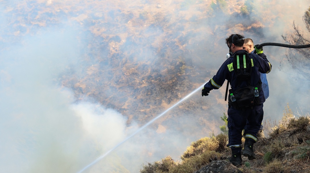 Πυροσβέστης με τη μάνικα ανά χείρας επιχειρεί για την κατάσβεσης φωτιάς