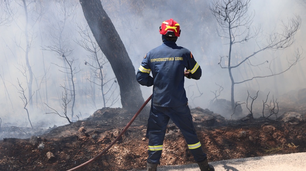 Πυροσβέστης με τη μάνικα ανά χείρας επιχειρεί για την κατάσβεσης φωτιάς