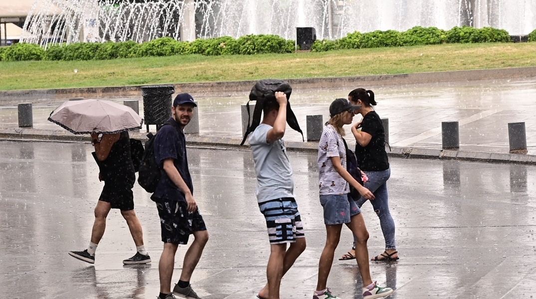 Πολίτες περπατούν εν μέσω βροχής