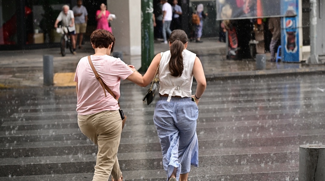 Βροχές και πολίτες που περπατούν στον δρόμο υπό βροχή