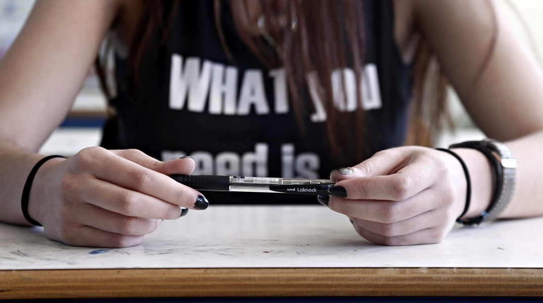 Μαθήτρια κρατά στυλό ενώ κάθεται στο θρανίο της