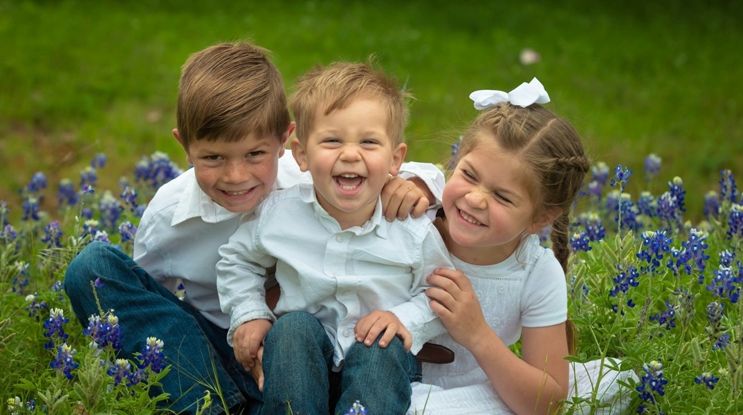 Τρία παιδιά ποζάρουν χαμογελαστά στον φακό