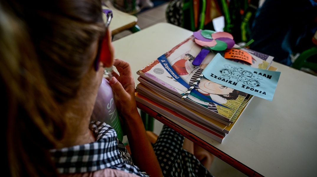 Μαθήτρια κάθεται στη θέση της έχοντας τα βιβλία της μπροστά της πάνω στο θρανίο και σημειώματα για καλή σχολική χρονιά