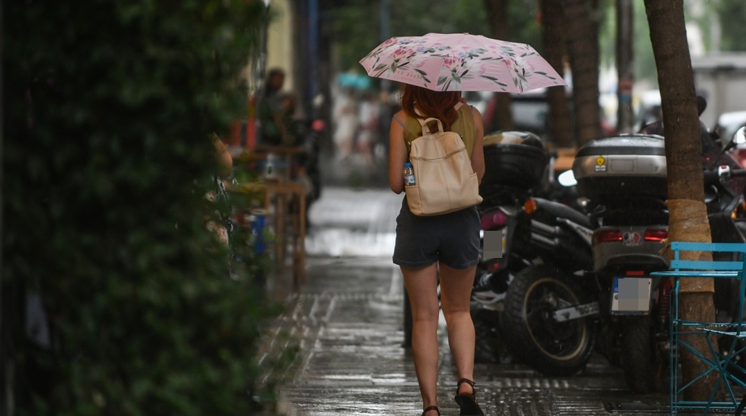 Γυναίκα με ομπρέλα προστατεύεται από τα πρωτοβρόχια