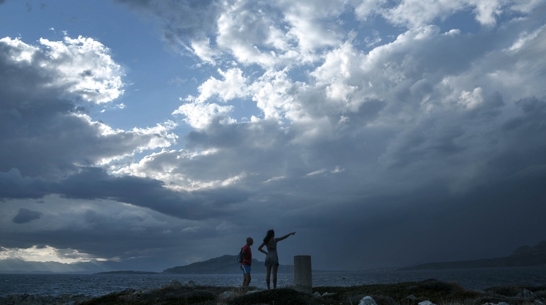 Δύο ατομα σε λόφο ενώ πίσω τους φαίνονται μαύρα σύννεφα