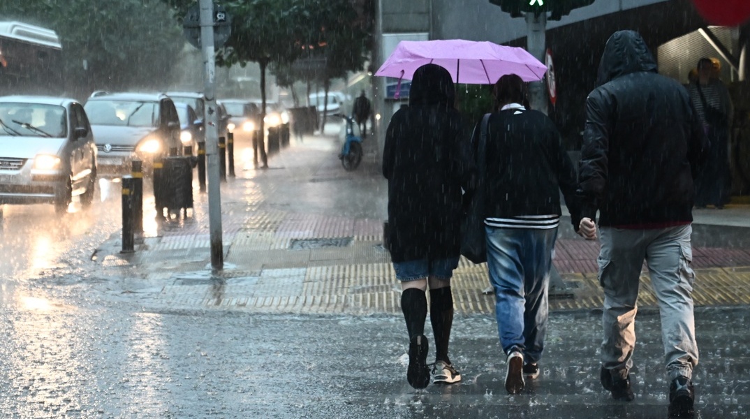 Πολίτες περπατούν εν μέσω βροχής σε δρόμο της Αθήνας