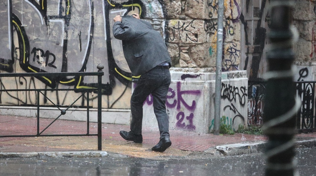 Άτομο σηκώνει το κουστούμι για να προστατευτεί από τη βροχόπτωση