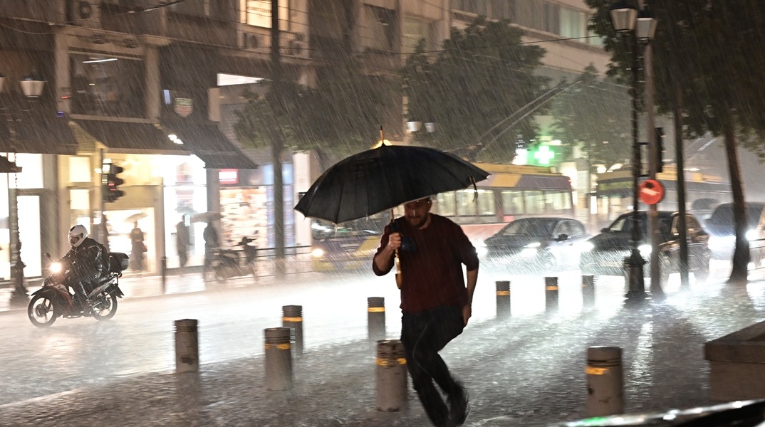 Πολίτης με ομπρέλα εν μέσω καταιγίδες και πλημμυρισμένων δρόμων