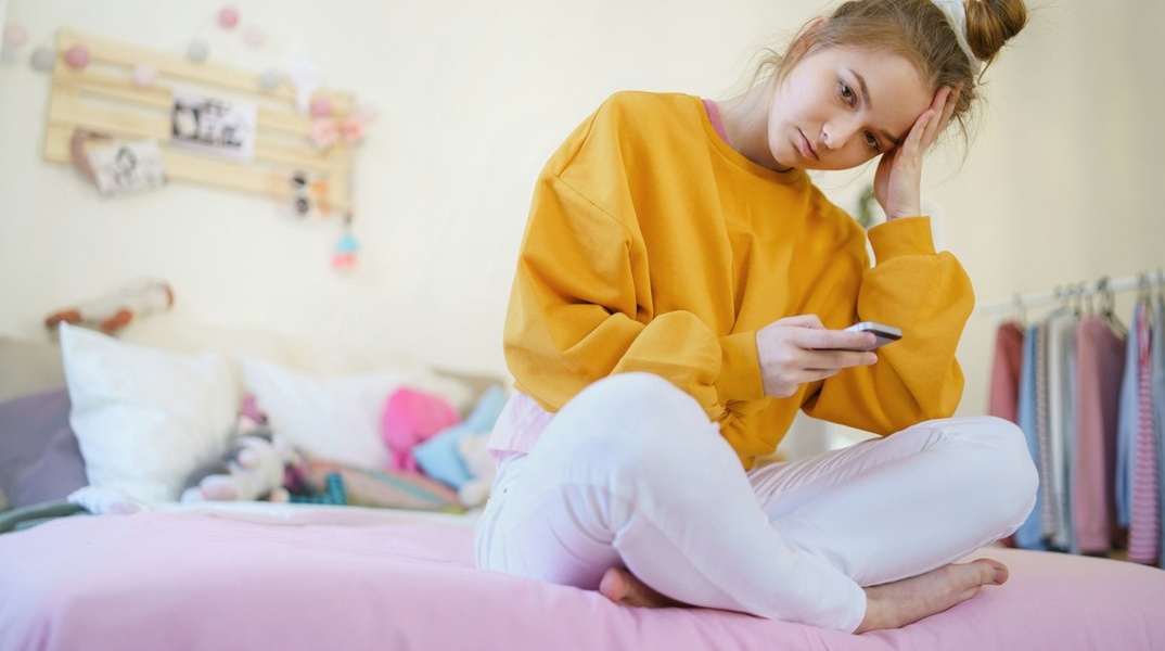 Έφηβη στεναχωρημένη στο δωμάτιο της κρατά και κοιτά κινητό