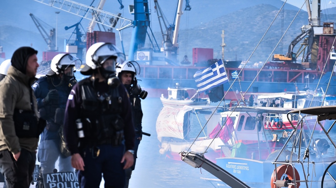 Αστυνομικές δυνάμεις στο λιμάνι του Βόλου και αλιείς που διαμαρτύρονται με τις συνθήματα και καπνογόνα από τις βάρκες τους