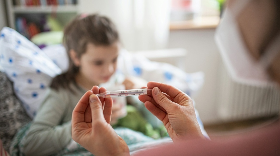 Παιδί με μάσκα και άτομο που του μετρά τη θερμοκρασία