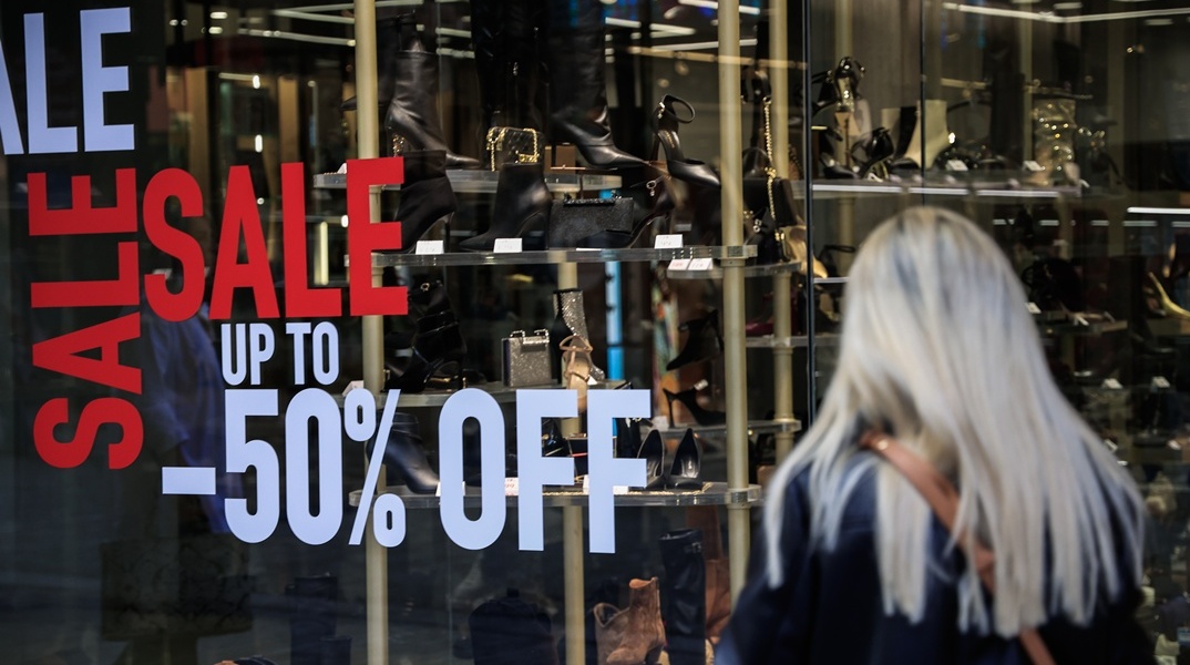 Γυναίκα μπροστά από βιτρίνα καταστήματος με αναφορά στις χειμερινές εκπτώσεις