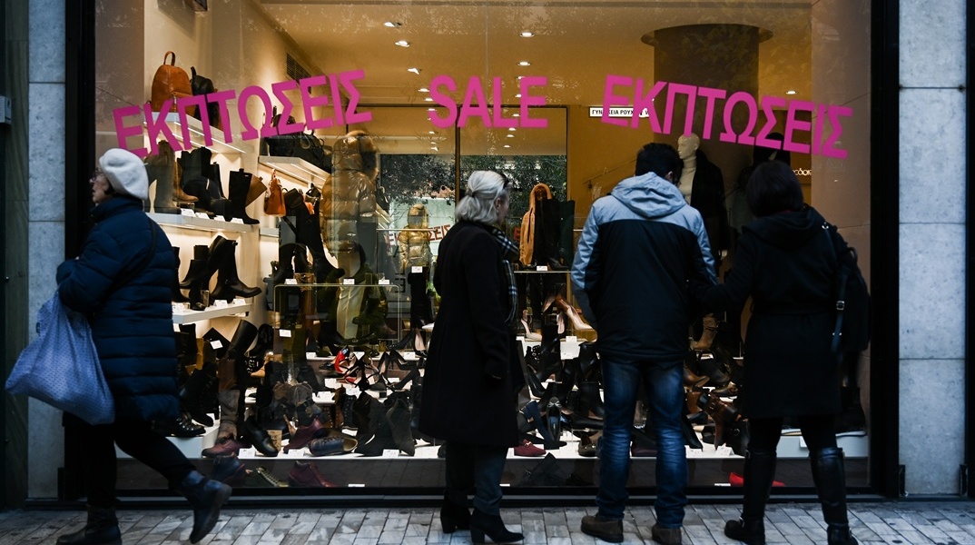 Βιτρίνα με ταμπέλα για χειμερινές εκπτώσεις και κόσμος που βλέπει τα προϊόντα