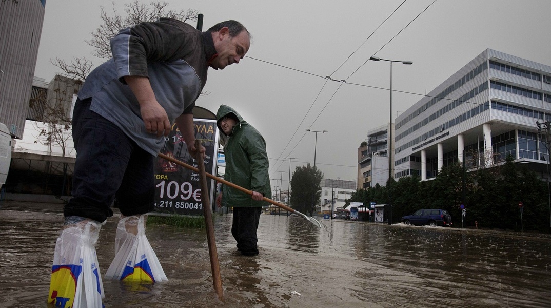 Πολίτες προσπαθούν να καθαρίσουν υπόνομο σε πλημμυρισμένο δρόμο στην Πειραιώς