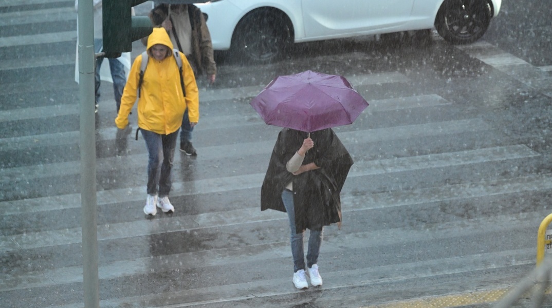 Πολίτες με ομπρέλες εν μέσω καταιγίδας σε δρόμο της Αθήνας