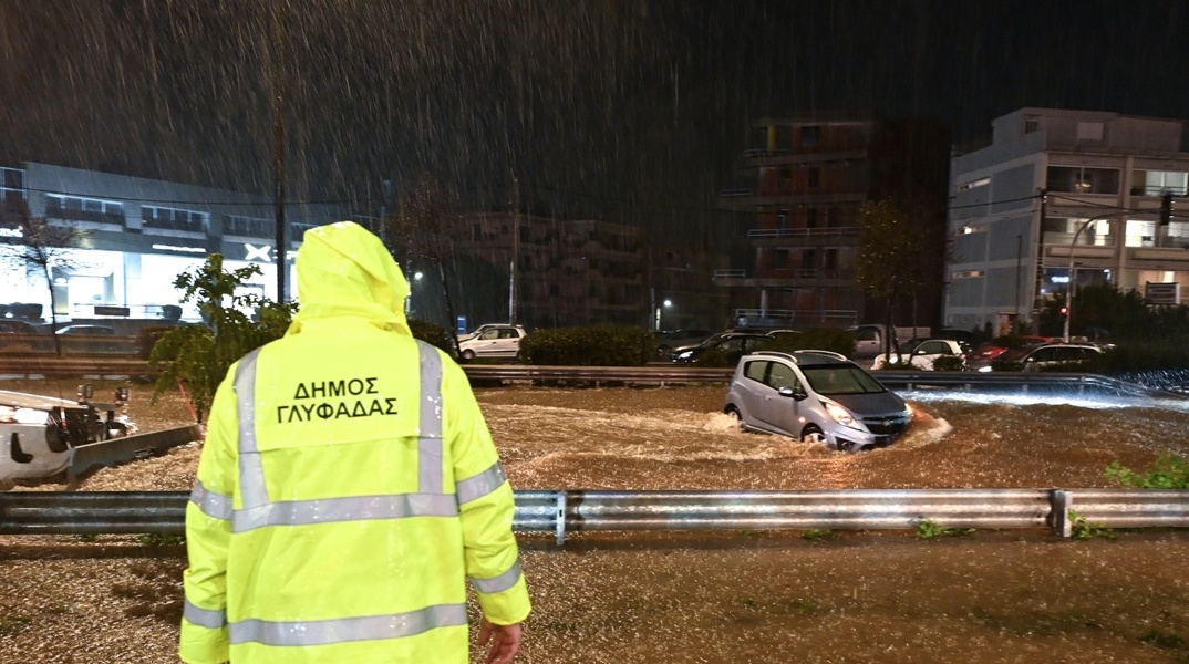 Υπάλληλος του δήμου Γλυφάδα σε σημείο δρόμου που έχει μετατραπεί σε ποτάμι