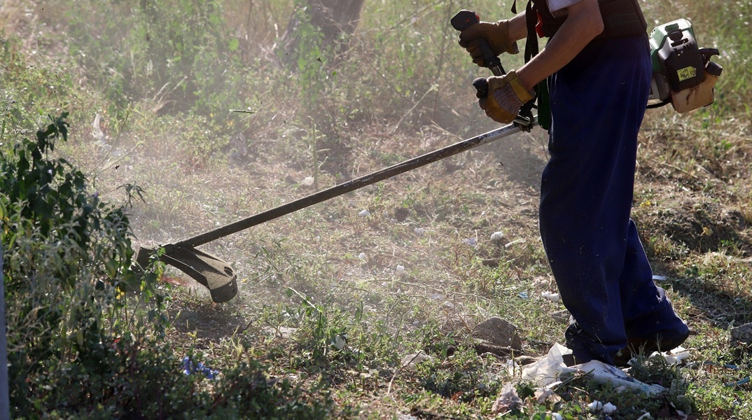 Άτομο με χορτοκοπτικό καθαρίζει οικόπεδο
