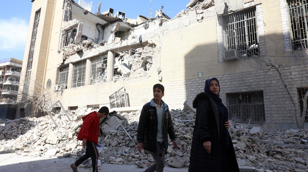 Γυναίκα με παιδιά περνούν μπροστά από τα συντρίμμια κτιρίου στην Τεχεράνη