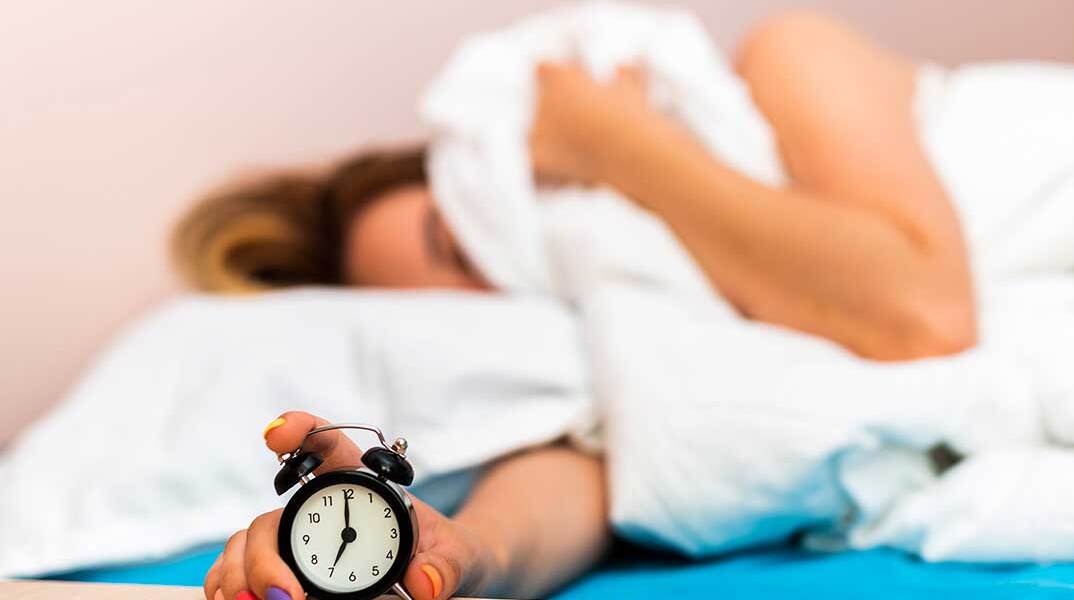 Γυναίκα στο κρεβάτι κλείνει το ξυπνητήρι