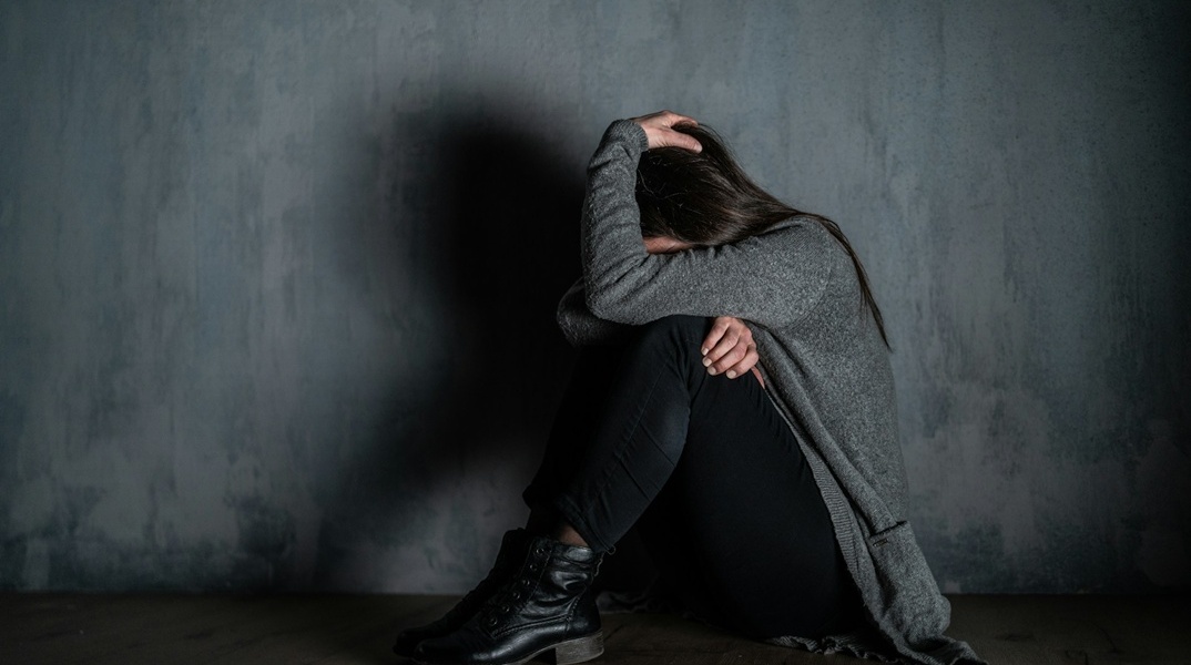 Γυναίκα κρύβει το πρόσωπό της ενώ είναι καθισμένη στο πάτωμα ενός σπιτιού