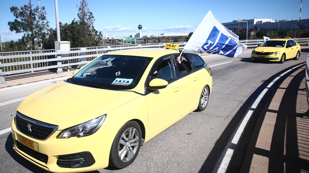 Οδηγός ταξί που οδηγεί και κρατά πανό με το λογότυπο του ΣΑΤΑ