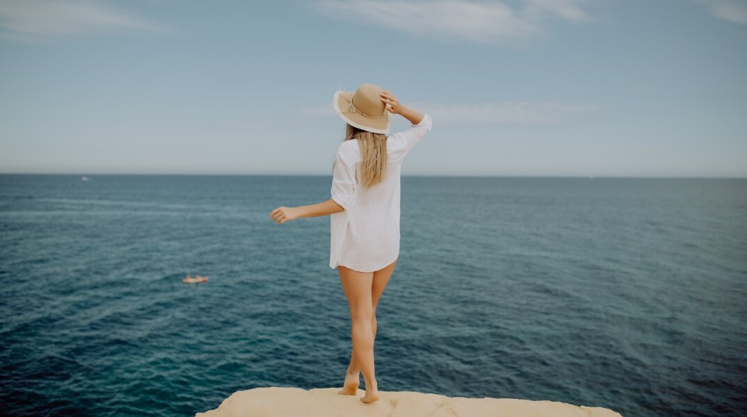 Γυναίκα με καπέλο μπροστά στη θάλασσα