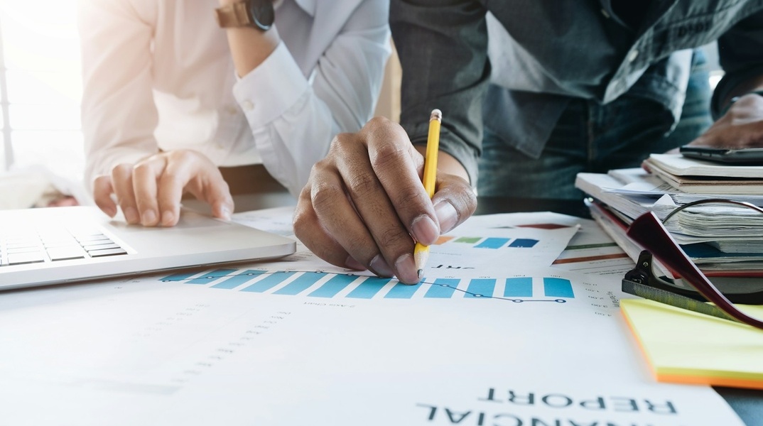 Έγραφα πάνω σε τραπέζι που γράφουν Financial Report και άτομα που τα μελετούν κάνοντας σημειώσεις με μολύβι