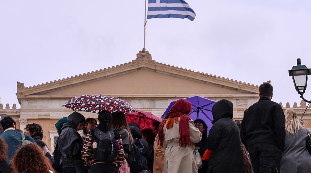 Πολίτες με ομπρέλες υπό βροχή μπροστά από τη Βουλή