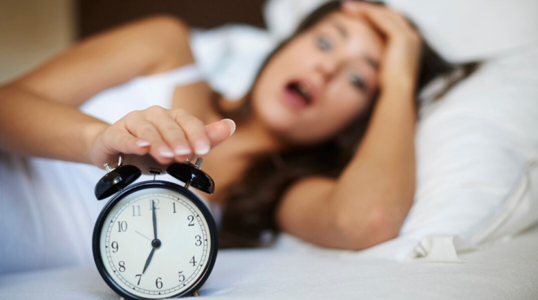 Γυναίκα ξυπνά το πρωί και πιάνει το ξυπνητήρι στο κρεβάτι