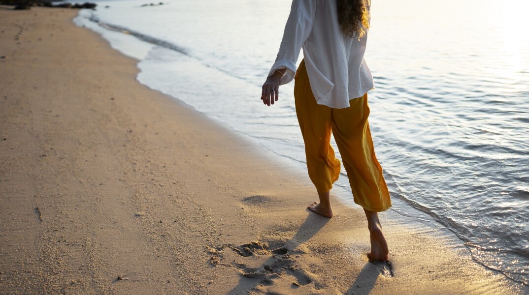 Γυναίκα περπατά ξυπόλυτη στην παραλία