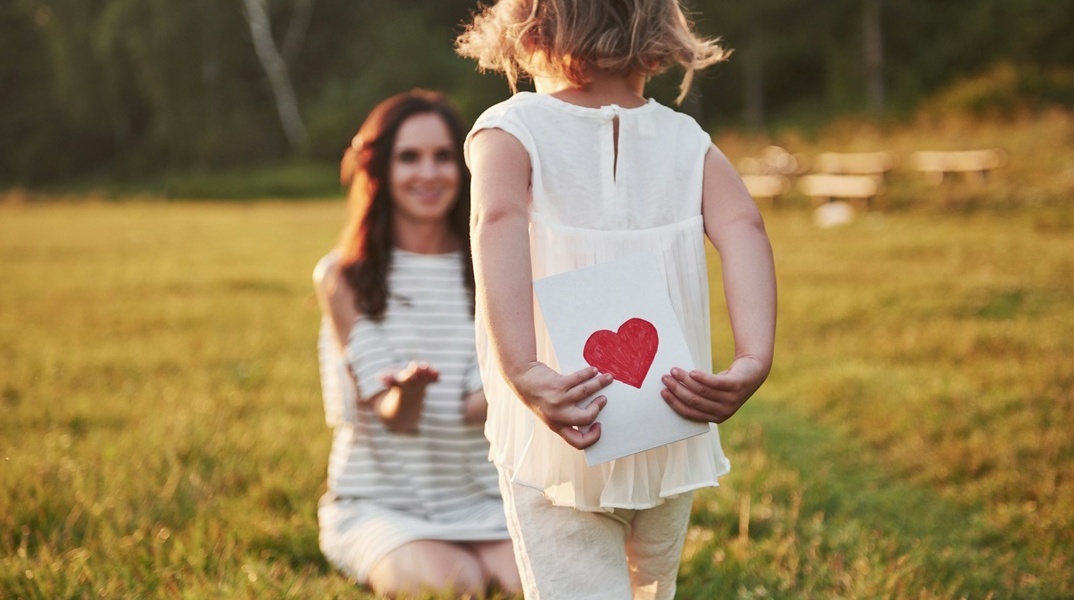 Κοριτσάκι τρέχει προς τη μητέρα του έχοντας κρυμμένη πίσω της μία καρδούλα