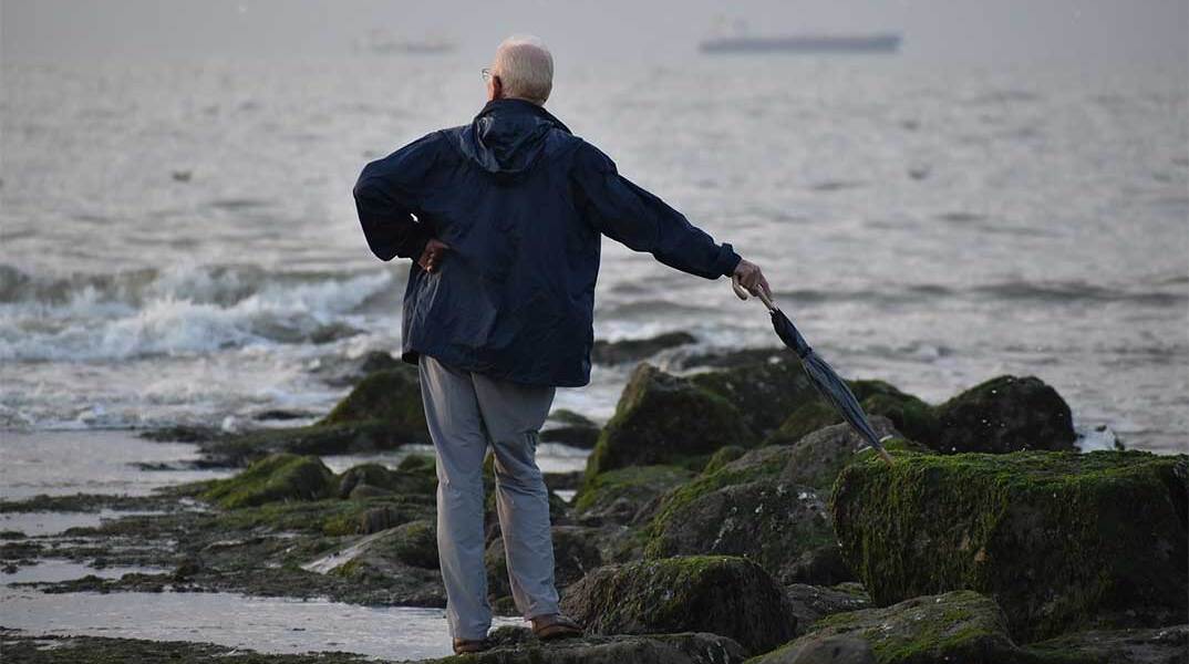 Ηλικιωμένος με ομπρέλα αγναντεύει τη θάλασσα
