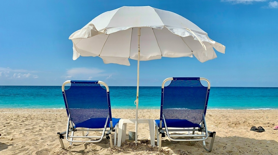 Παραλία στη Λευκάδα με δύο ξαπλώστρες και μία ομπρέλα καρφωμένη στην άμμο