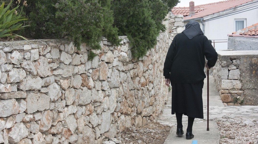 Ηλικιωμένη με μπαστούνι περπατά σε σοκάκι