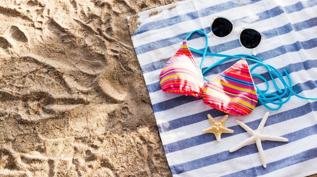 Μαγιό, γυαλιά ηλίου και αστερίες σε πετσέτα θαλάσσης στην άμμο