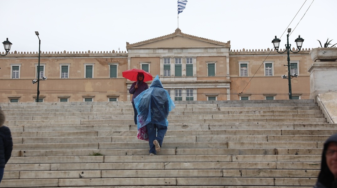 Πολίτες με ομπρέλα και αδιάβροχο μπροστά στη Βουλή