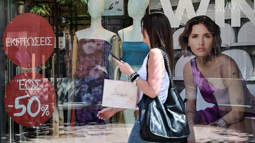 Γυναίκα με τσάντα περνά έξω από κατάστημα εν μέσω εκπτώσεων