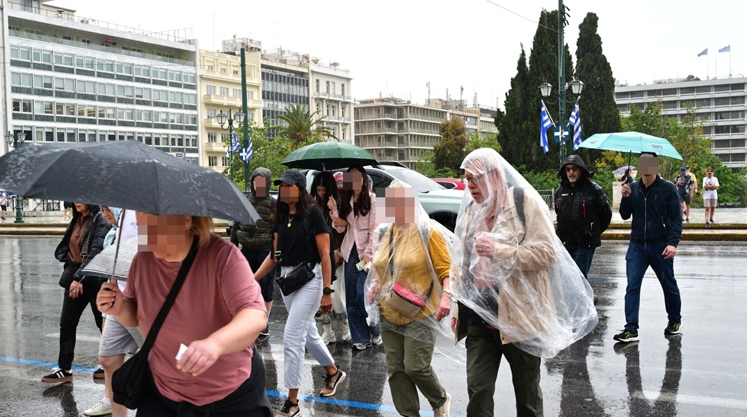 Πολίτες με ομπρέλες ανά χείρας προστατεύονται από τη βροχή