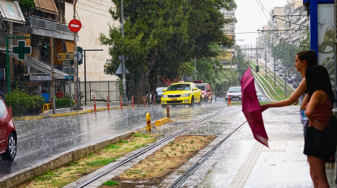 Βροχή και κοπέλες που κλείνουν την ομπρέλα τους σε στάση τραμ