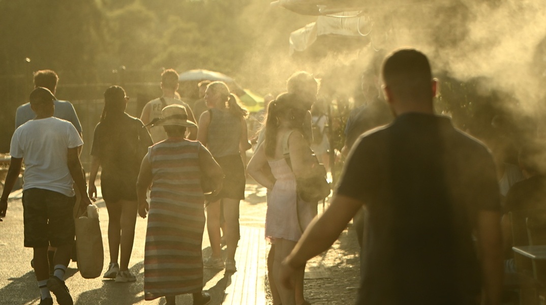 Πολίτες περνούν από ανεμιστήρες που ρίχνουν νερό
