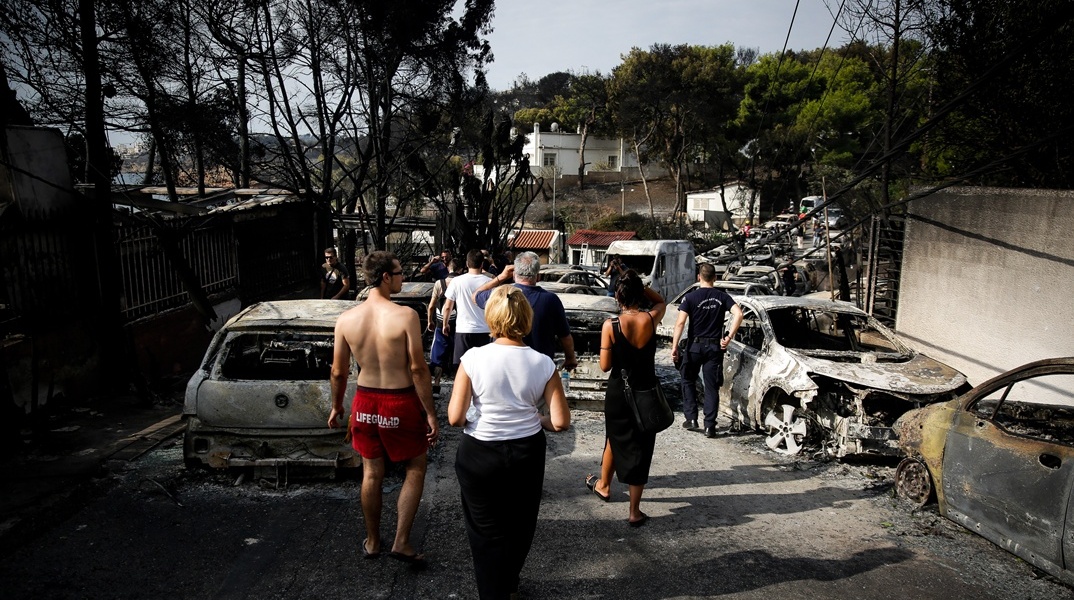 Πολίτες περπατούν ανάμεσα σε καμένα οχήματα την επομένη της τραγωδίας στο Μάτι