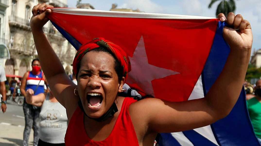 Γυναίκα με τη σημαία της Κούβας στα χέρια διαδηλώνει στον δρόμο