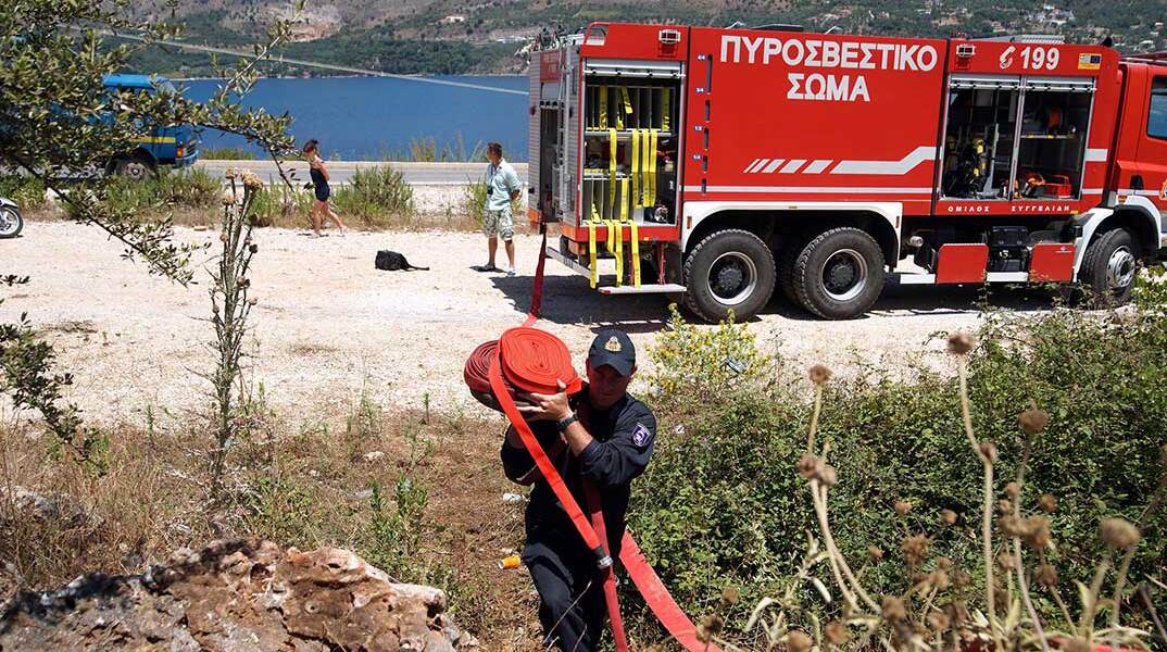 Πυροσβέστης μεταφέρει μάνικα μπροστά από πυροσβεστικό όχημα