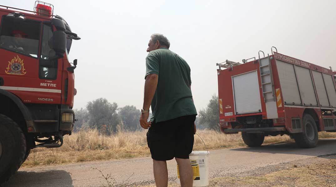 Εθελοντής δίπλα σε πυροσβεστικά οχήματα για να βοηθήσει σε δασική πυρκαγιά