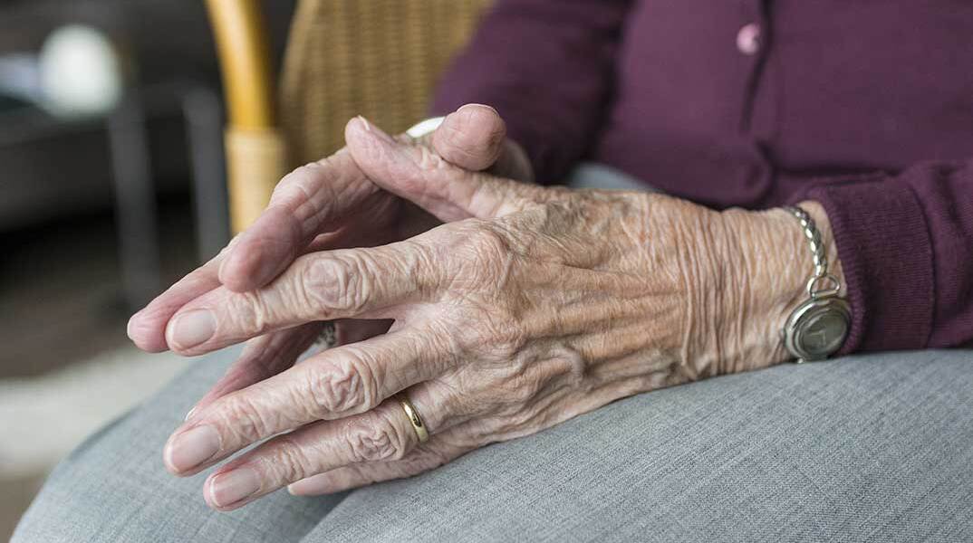 Ηλικιωμένη έχει ενώσει τα δάχτυλα των χεριών της πάνω στα γόνατά της