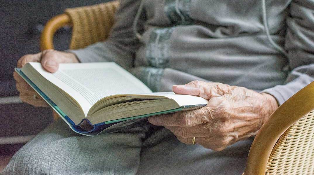 Ηλικιωμένη διαβάζει βιβλίο στην καρέκλα