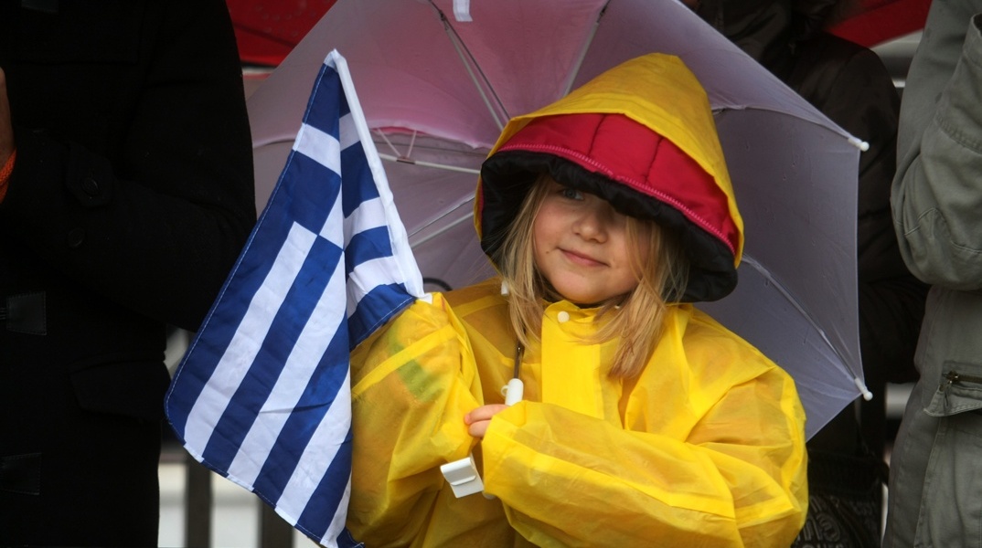 Κοριτσάκι με ομπρέλα και την ελληνική σημαία σε παρέλαση