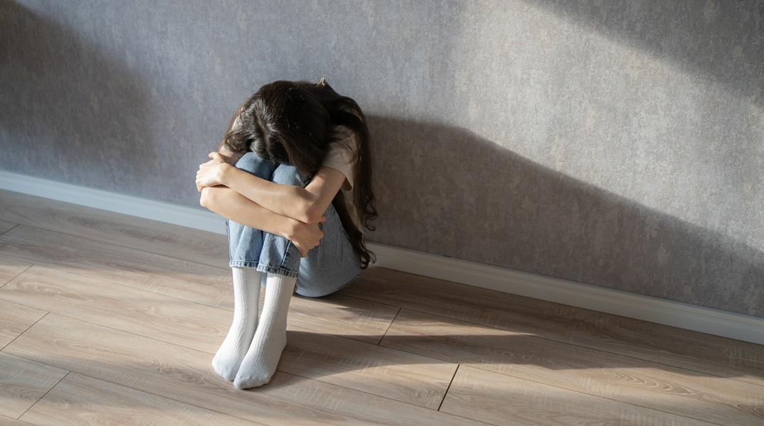 Ανήλικη με κρυμένο το πρόσωπο κάθεται στο πάτωμα σπιτιού