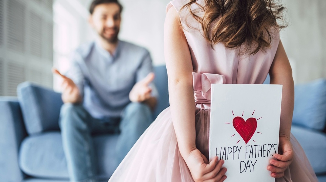 Κοριτσάκι με ζωγραφιά για τη γιορτή του πατέρα που την κρύβει πίσω από την πλάτη της όσο κατευθύνεται προς τον πατέρα της