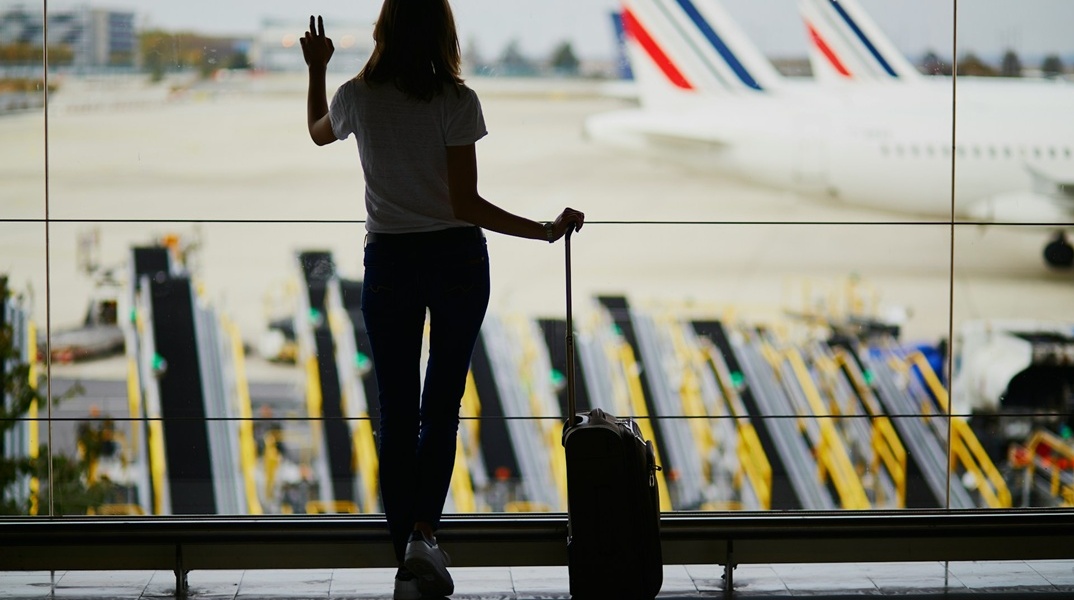 Γυναίκα με τη βαλίτσα της στο τζάμι αεροδρομίου